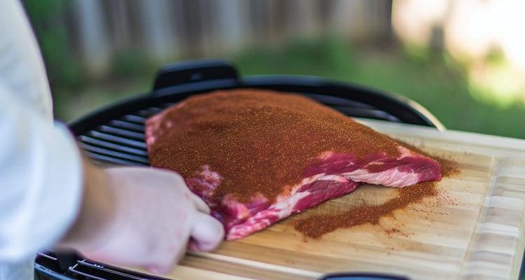 applying brisket rub to raw beef brisket on cutting board, generous coating of reddish-brown spice rub visible - cooking process applying brisket rub to raw beef brisket on cutting board, generous coating of reddish-brown spice rub visible - cooking process