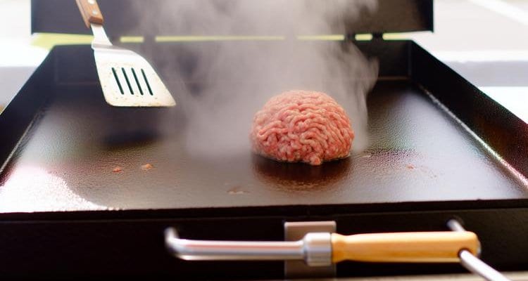 Ground beef ball on Blackstone griddle surface before smashing with spatula nearby Ground beef ball on Blackstone griddle surface before smashing with spatula nearby