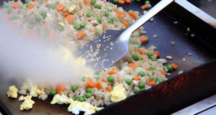 Fried rice with colorful vegetables being stirred on Blackstone griddle with metal spatula and sesame seeds Fried rice with colorful vegetables being stirred on Blackstone griddle with metal spatula and sesame seeds