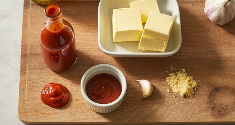 Bottle of cayenne pepper hot sauce and sticks of butter arranged on a wooden board for homemade Buffalo sauce Bottle of cayenne pepper hot sauce and sticks of butter arranged on a wooden board for homemade Buffalo sauce