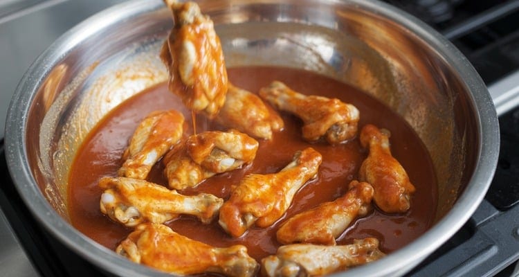 Freshly cooked chicken wings being tossed in warm Buffalo sauce inside a large metal mixing bowl Freshly cooked chicken wings being tossed in warm Buffalo sauce inside a large metal mixing bowl