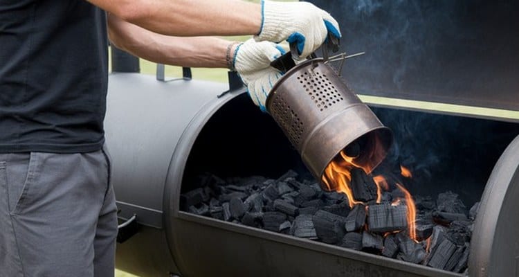 Pouring Lit Charcoal into the Firebox Gloved hands pouring lit charcoal into an offset smoker firebox