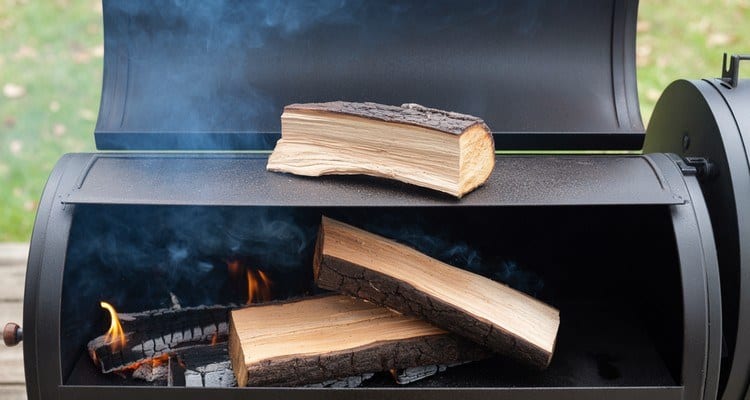 Prewarming a Wood Split on the Firebox Single hardwood split prewarming on an offset smoker firebox with a fire below