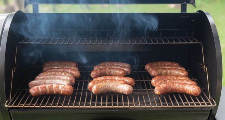 Uncooked brats spaced on pellet grill grates with thin blue smoke rising Uncooked brats spaced on pellet grill grates with thin blue smoke rising