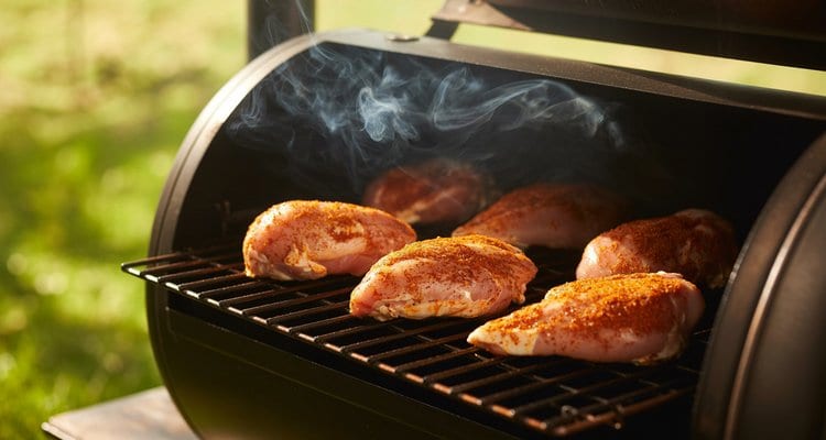 Chicken Breasts on Smoker Grates Seasoned raw chicken breasts with spice rub on smoker grates with white smoke rising