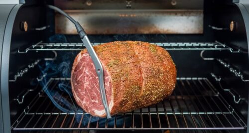 Seasoned eye of round roast smoking on grill grates with thermometer probe