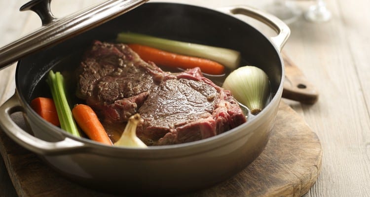 Braised Chuck Steak in Dutch Oven — Fork-Tender Oven Method Dutch oven with the lid off showing chuck steak braising in dark liquid with carrots, onion, and celery