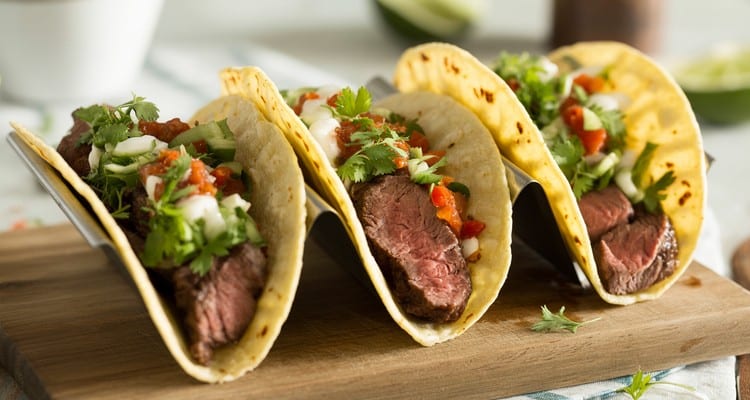 Chuck Steak Tacos — Shredded Smoked or Braised Beef on Corn Tortillas Three chuck steak tacos on a plate topped with diced onion, cilantro, and cotija with a lime wedge