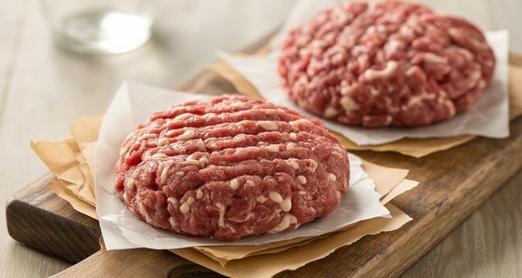 Formed beef pork burger patties ready to chill Perfectly formed raw beef and pork burger patties on parchment paper with dimples pressed in the center