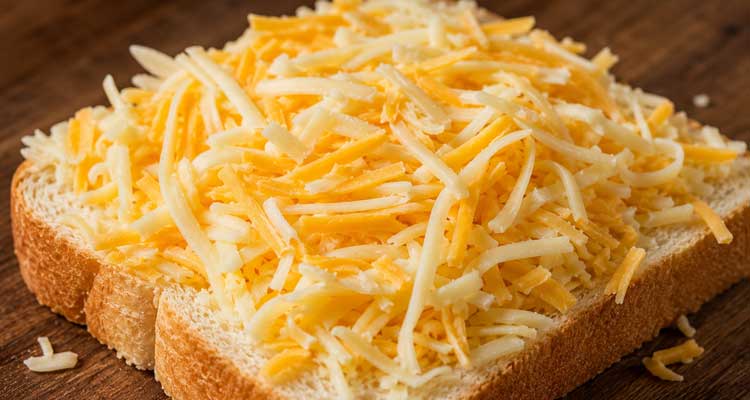 Freshly shredded blend of American and Gruyere cheese piled on a slice of thick-cut white bread before cooking