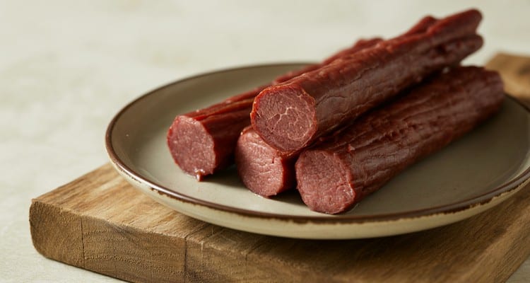 Close up of sliced smoked beef sticks showing firm reddish interior on a plain plate Close up of sliced smoked beef sticks showing firm reddish interior on a plain plate